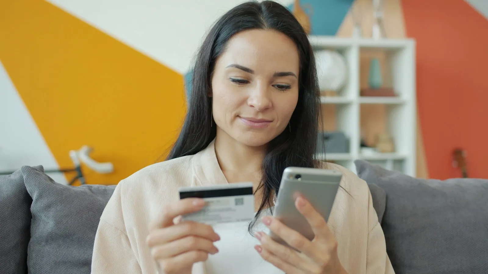 Woman on a couch shopping online with her smartphone and a credit card
